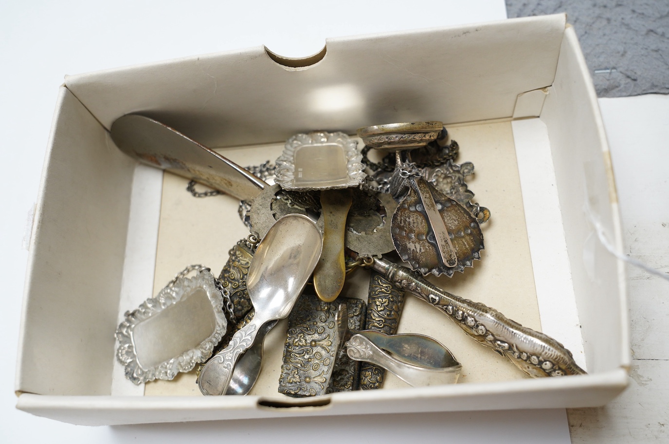 Three assorted modern silver wine labels, a ceramic wine label, a pair of silver pepperettes, a silver topped glass toilet jar, a Dutch white metal sifter spoon and seven plated items including a pair of peacock menu hol